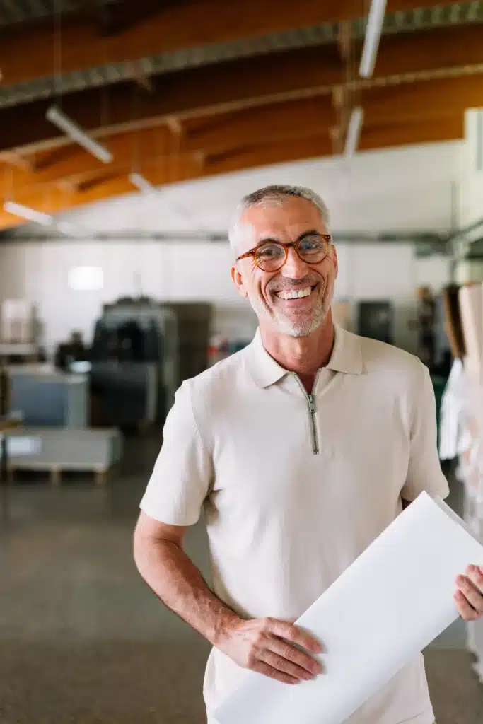 Portrait of good-looking senior man with glasses working in printing office, looking at camera and smiling