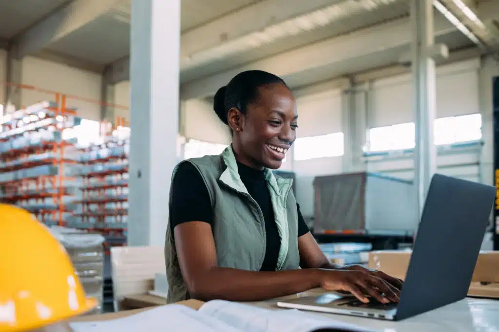 Portrait of beautiful young woman working in factory, using laptop