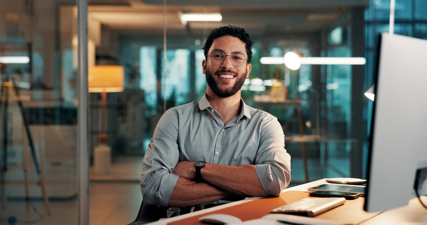 Arms crossed, portrait and smile of designer man at desk in office for complete task or satisfaction. About us, confident and creative with happy employee in design workplace for online development